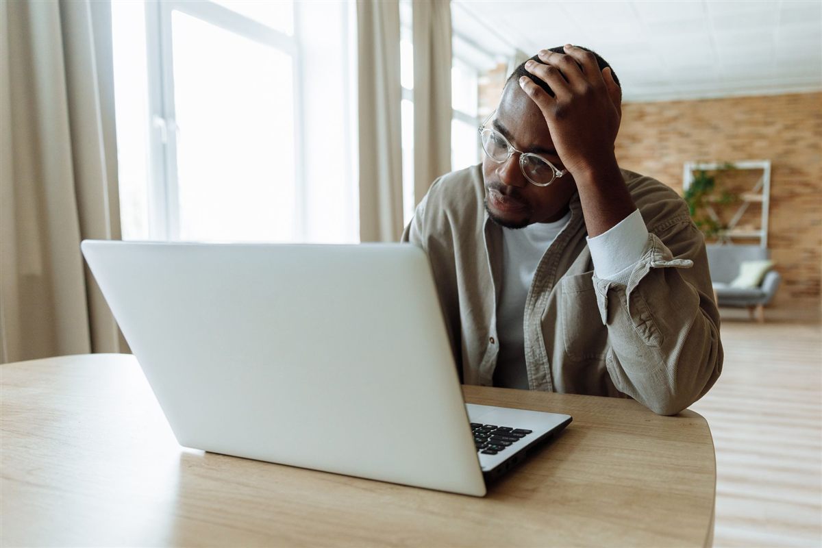 A frustrated person with their head in their hand, looking at a laptop screen